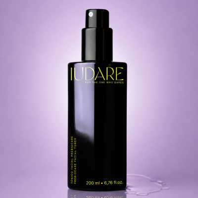 Frasco preto de tónico facial prebiocare com texto amarelo sobre superfície lilás refletora.