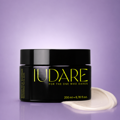 Frasco preto de máscara facial com creme branco ao lado sobre fundo lilás