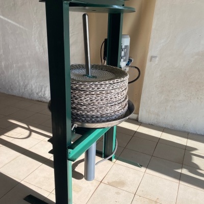 Máquina industrial verde com carretel e motor num chão de azulejos claros