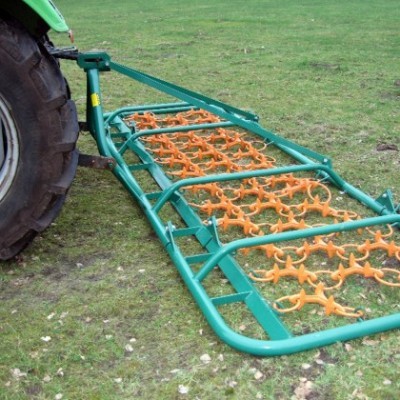 Arado agrícola verde metálico com peças laranjas ligado a trator no campo