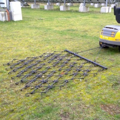 Rede de arrasto preta ligada a veículo amarelo em terreno com relva