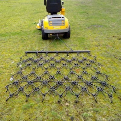 Trator amarelo com acessório metálico para controlo de ervas daninhas sobre relvado