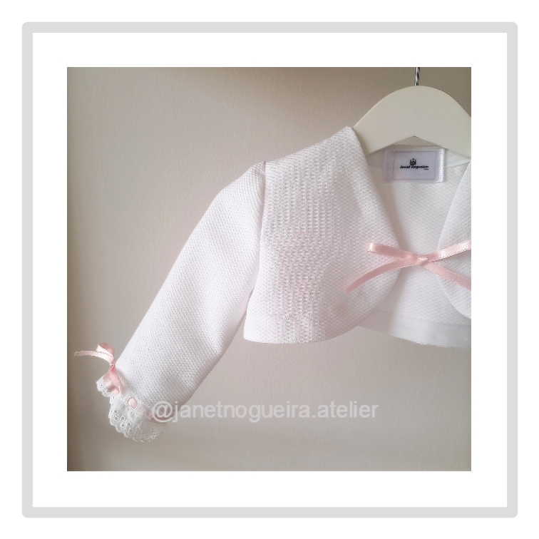 Bolero Bianca Bolero branco com laço rosa pendurado num cabide branco