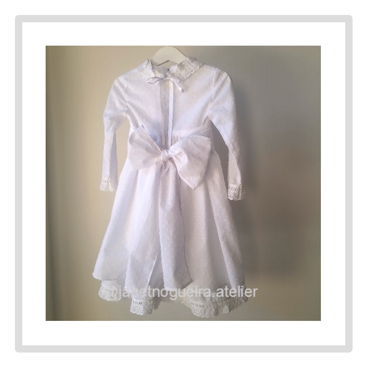Vestido Iria Vestido branco infantil com laço e renda pendurado num cabide