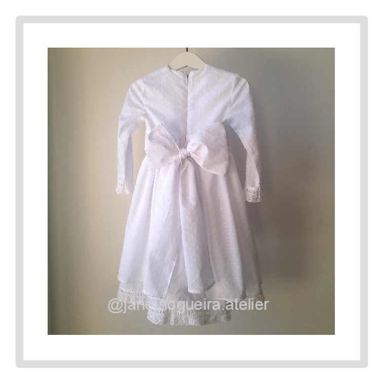 Vestido Iria Vestido branco de menina com laço e acabamento em renda pendurado num cabide