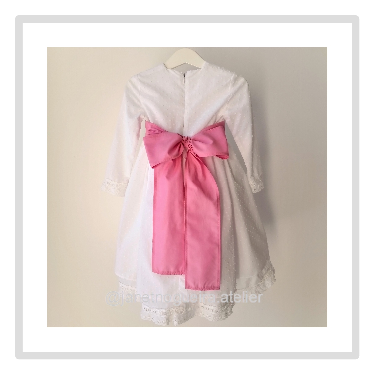 Vestido Iria Vestido branco de criança com laço rosa pendurado em cabide