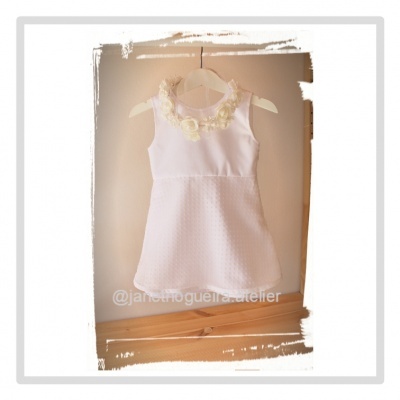 Vestido branco de criança com flores bege no decote pendurado num cabide