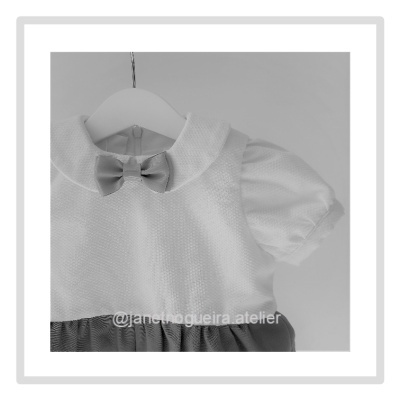 Vestido de bebé branco com laço e saia escura em cabide branco