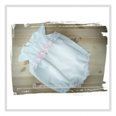Pelele branco para bebé com renda e fita rosa sobre madeira clara