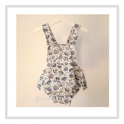 Jardineira de bebé branca com padrão azul de folhas pendurada num cabide