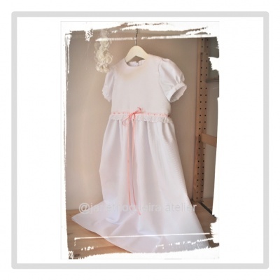Vestido branco de criança com laço cor de rosa e detalhes de renda