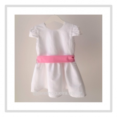Vestido infantil branco com faixa rosa pendurado em cabide