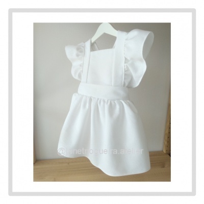 Vestido branco infantil com folhos nas costas pendurado num cabide