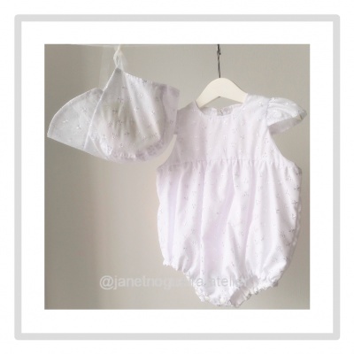 Conjunto de bebé branco com body e chapéu bordados, pendurados num cabide branco