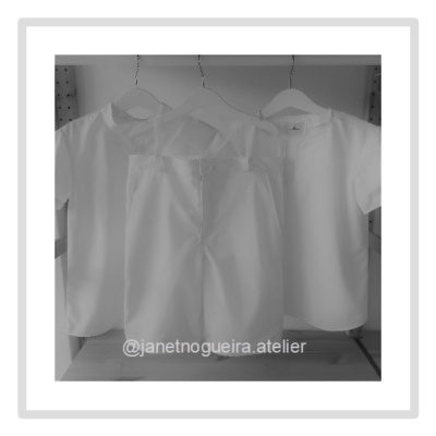 Três roupas brancas penduradas em cabides numa estrutura de madeira clara