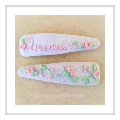 Dois ganchos de cabelo brancos bordados com flores cor-de-rosa e verdes.