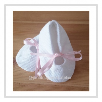 Sapatinhos de bebé brancos com fita rosa e botão sobre madeira clara