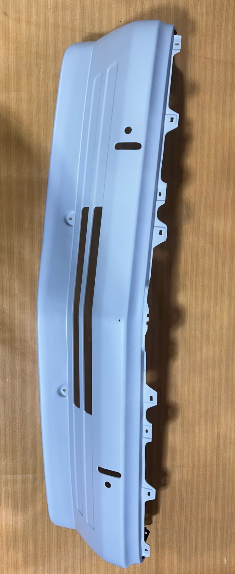 Peça branca de automóvel com encaixes sobre superfície de madeira clara