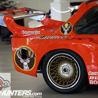 Parte traseira de carro de corrida vermelho com logotipos e roda dourada