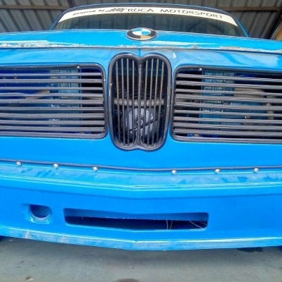 Frente de carro clássico azul com faróis circulares e grelha preta em oficina