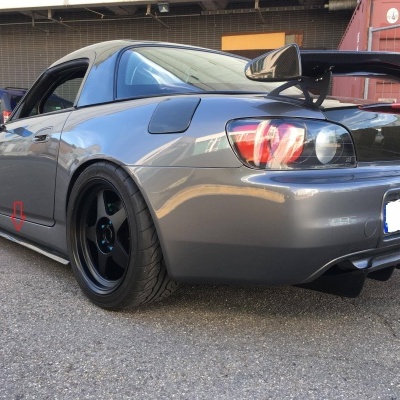 Carro desportivo cinza metálico com jantes e capota pretas, spoiler traseiro e ambiente industrial