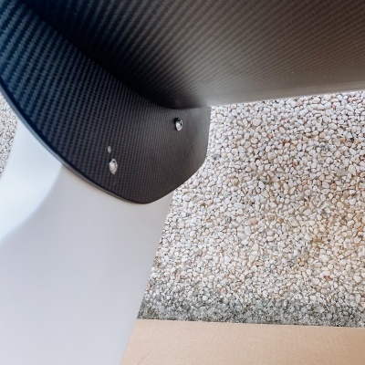 Estrutura branca com componente em fibra de carbono e parafusos sobre pedras brancas e chão bege