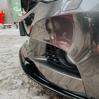 Parte dianteira de carro cinzento com farol e grelha preta em ambiente exterior