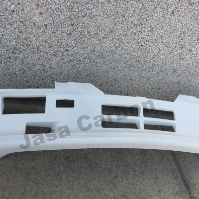 Para-choques frontal branco de automóvel com aberturas retangulares sobre chão de cimento