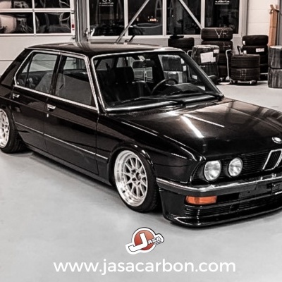 Automóvel sedan preto com jantes brancas numa oficina com pneus ao fundo