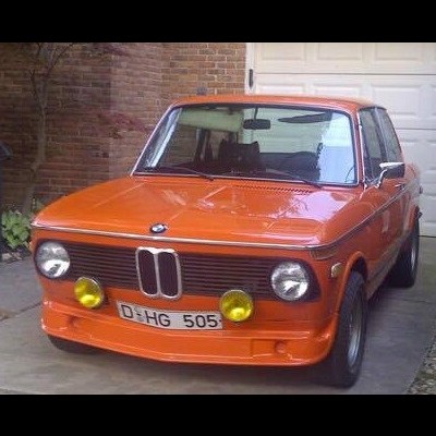 Carro clássico BMW laranja com faróis redondos e luzes amarelas adicionais