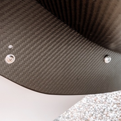 Superfície em fibra de carbono com três elementos metálicos e fundo de seixos cinzentos