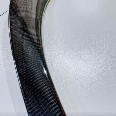 Peça automóvel em fibra de carbono com acabamento brilhante e padrão visível.