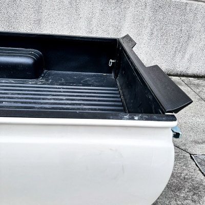 Caçamba preta de carrinha branca com parede de cimento ao fundo