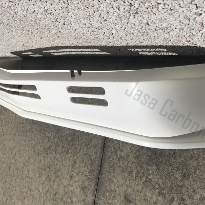 Parachoques branco com aberturas e texto Jasa Carbon junto a parede