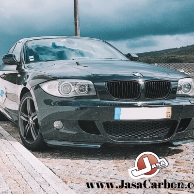 Carro BMW preto estacionado com céu nublado e publicidade no canto inferior direito