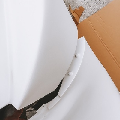 Peça branca com botões sobre chão de cimento e caixa de cartão