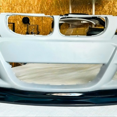 Para-choques dianteiro branco com detalhes pretos sobre superfície branca e fundo de madeira OSB