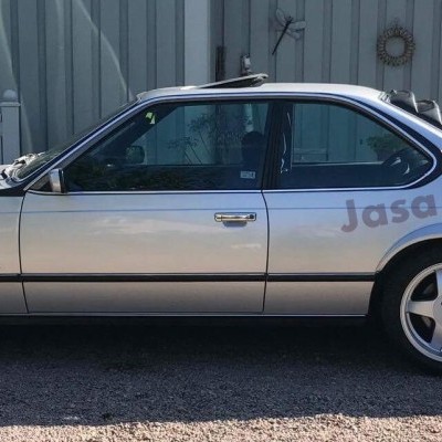 Carro coupé prateado com jantes de cinco braços e inscrição 'Jasa Carbon' no vidro, junto a edifício e relvado