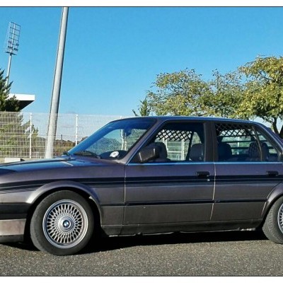 Carro sedan cinza escuro em parque com jantes prateadas e fundo de árvores e cerca