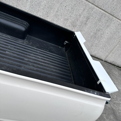 Caixa de carga de carrinha pick-up branca com parede preta e fundo riscado em local exterior de betão