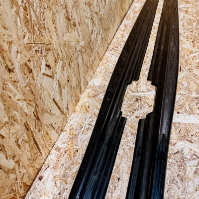 Duas peças longas pretas sobre painel de madeira aglomerada clara