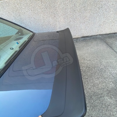 Carro azul metálico com aerofólio preto fosco na tampa da mala e mão segurando aerofólio