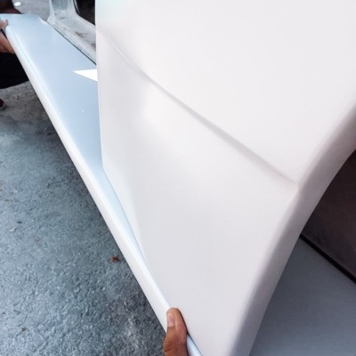 Peça branca rígida sendo segurada sobre superfície cinza perto de estrutura metálica