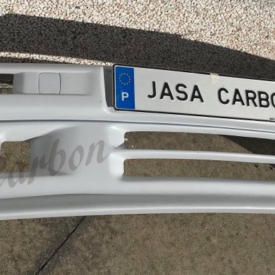 Para-choques de carro branco com etiqueta JASA CARBON sobre chão em pedra clara