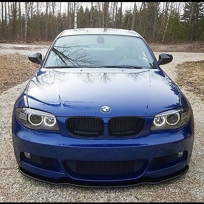 Carro azul BMW visto de frente em estrada de cascalho com árvores ao fundo