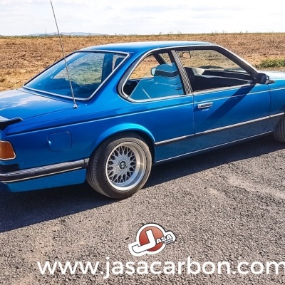 Carro desportivo clássico azul estacionado numa estrada com campo ao fundo