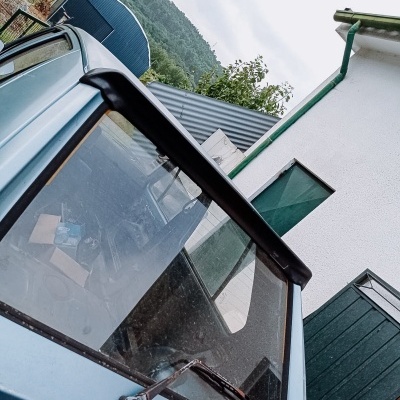 Carrinha azul claro com janela traseira e limpa-vidros, junto a edifício branco com portas e janelas verdes