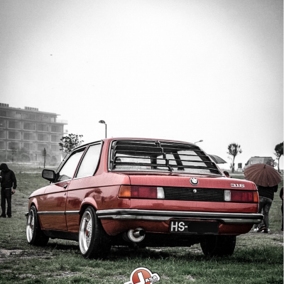 BMW 316 vermelho metalizado estacionado em relva com persiana traseira preta