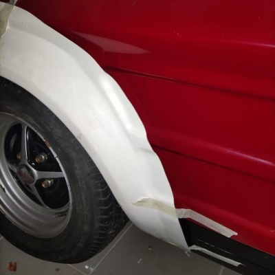 Carro vermelho com pneu e para-lamas branco com fita adesiva num chão de azulejos