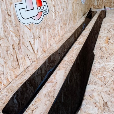 Peças longas pretas brilhantes sobre superfície de madeira OSB com logo JASA CARBONS na parede